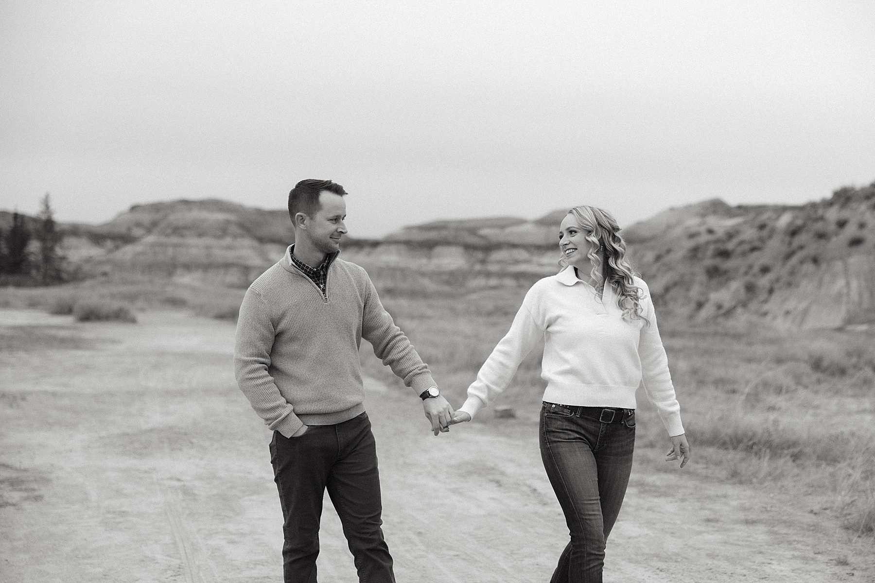 a couple wearing jeans with sweaters holding hands and smiling while looking at each other