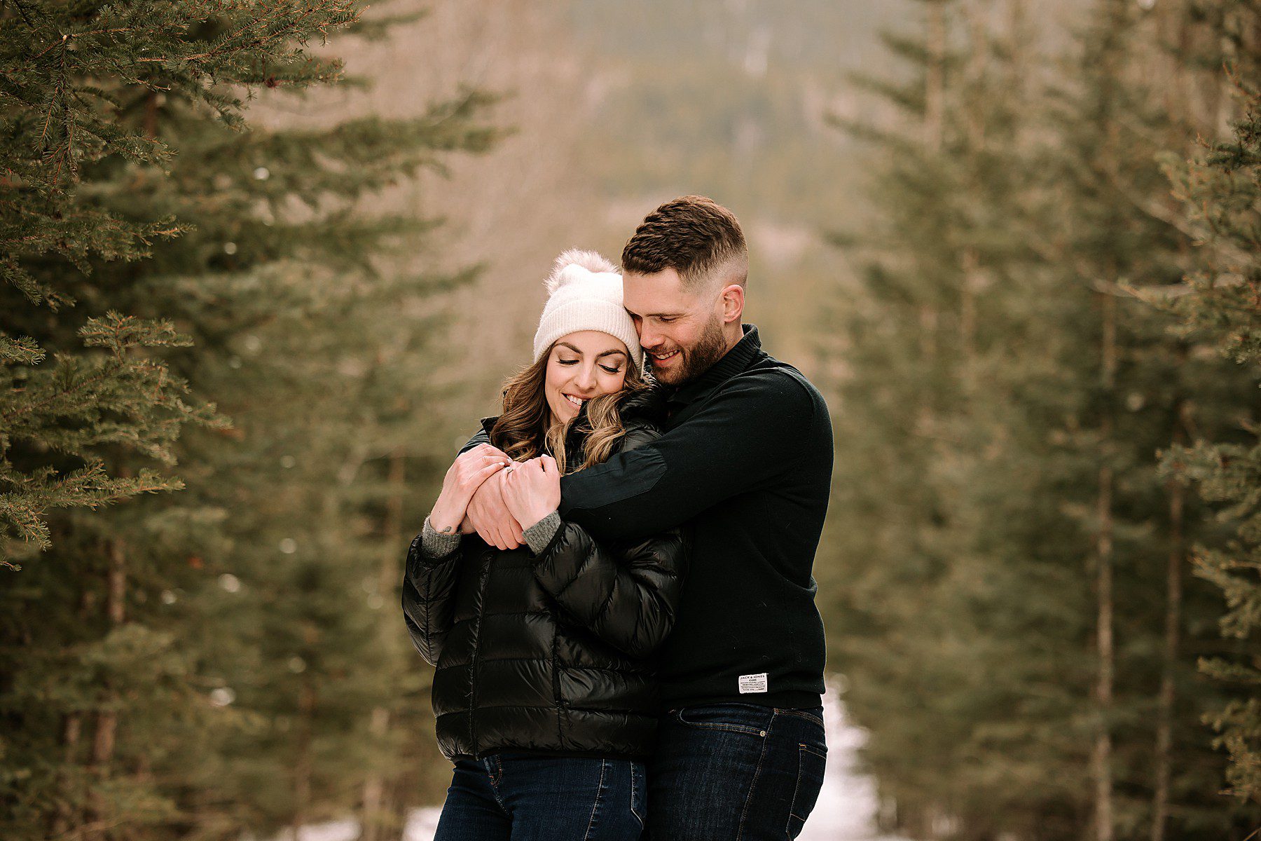 couple wearing winter outfits while standing in the snow surrounded by trees