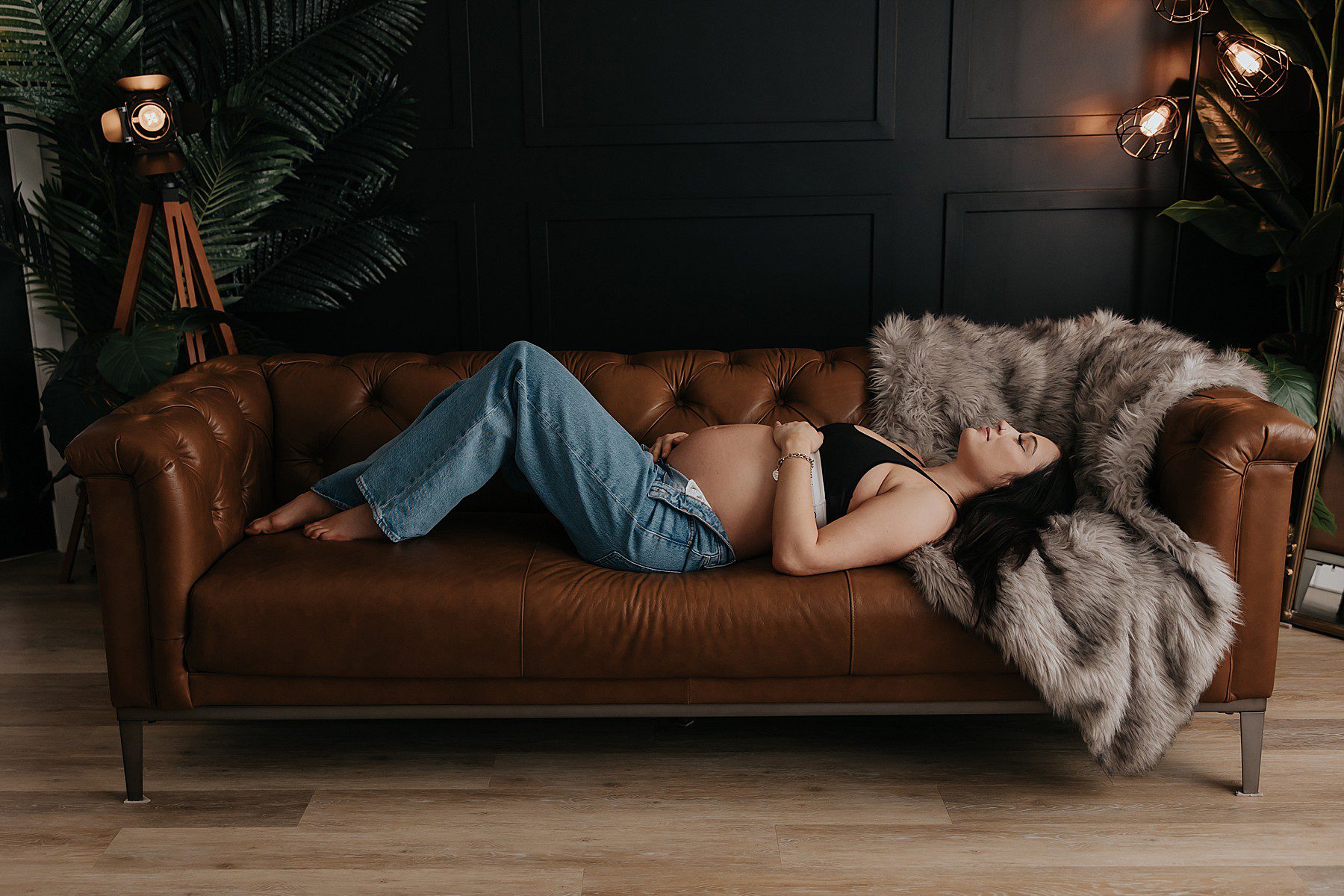 woman posing in a studio for maternity photos. She is wearing jeans with the top button undone and a black calvin klein bra