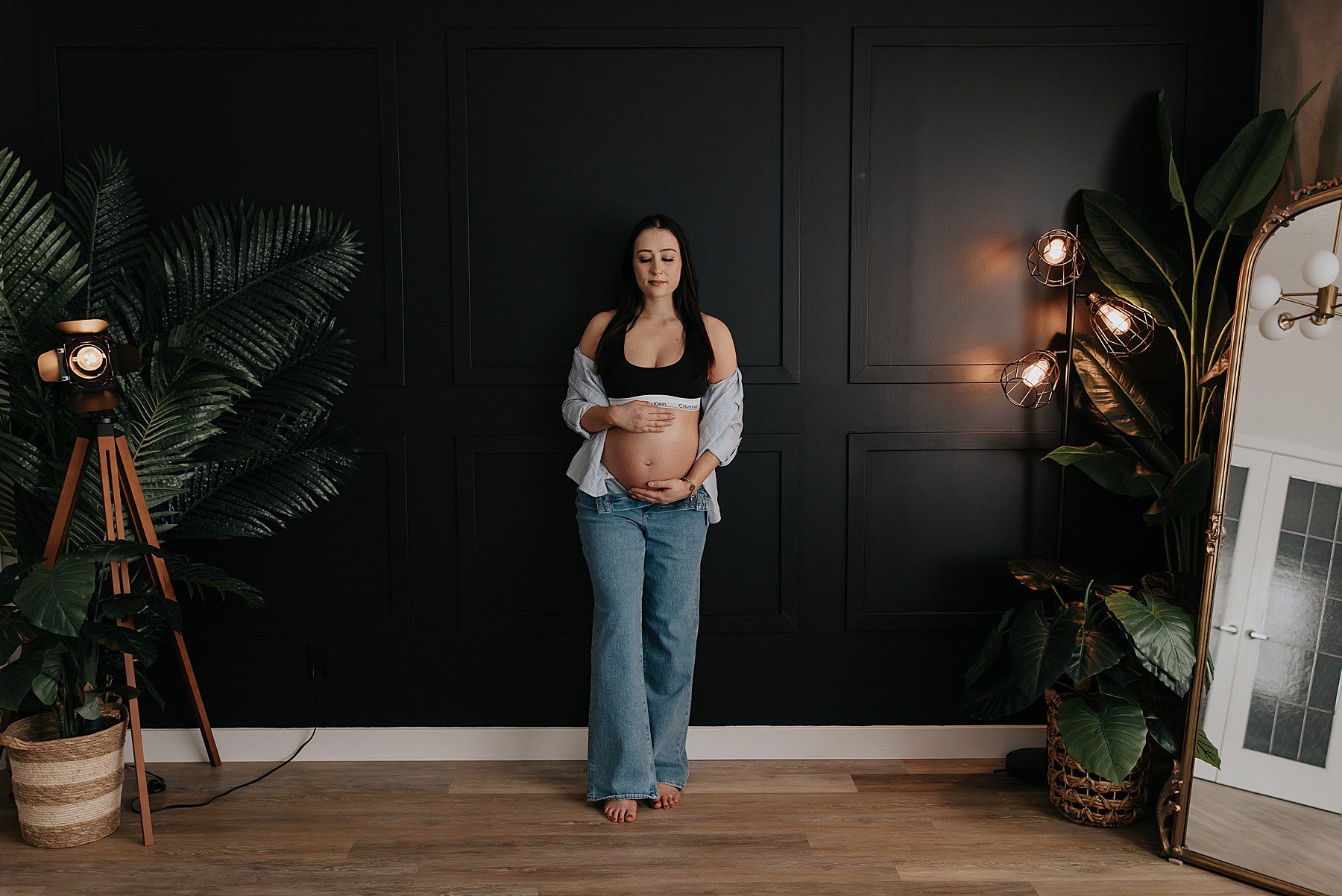 woman posing in a studio for maternity photos. She is wearing jeans with the top button undone and a black calvin klein bra