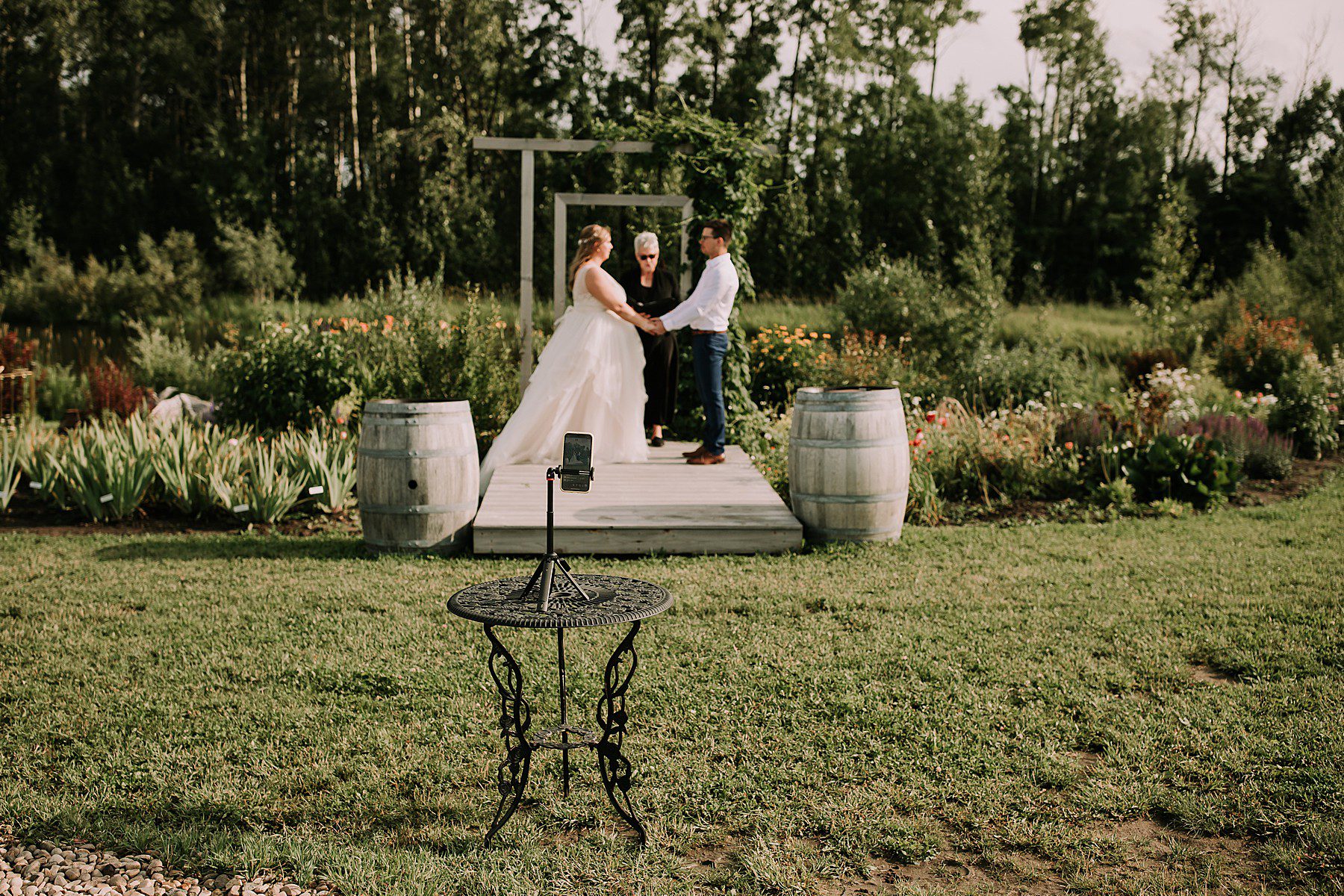 women dressed in a wedding dress and man dressed in dress pants and white shirt. They are standing at the wedding alter surrounded by nature
