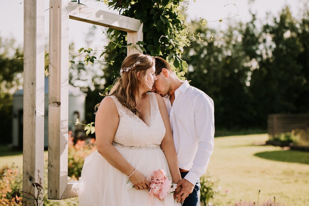 bride and groom standing in nature and snuggling close while posing for wedding photos. 