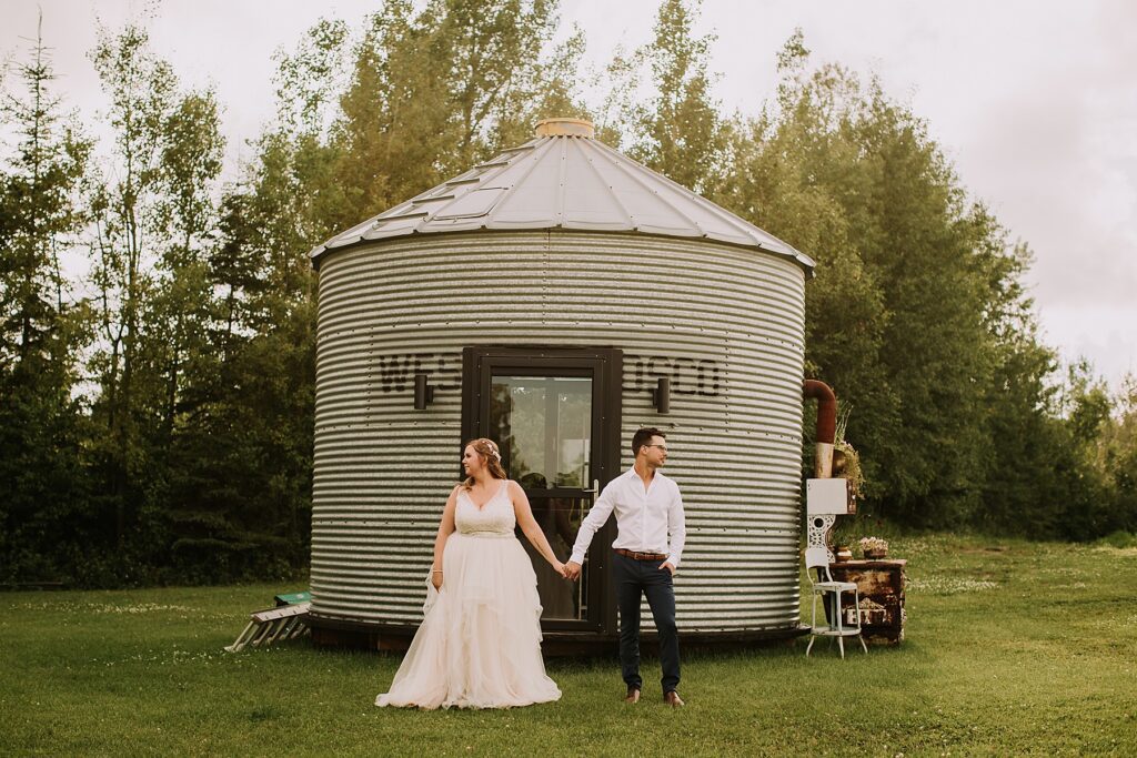 bride and groom standing in nature and snuggling close while posing for wedding photos. 
