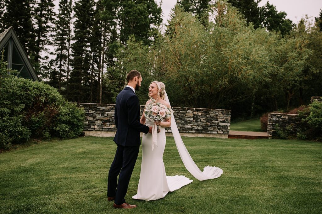 bride & groom standing in a green space sharing an intimate moment in their wedding attire